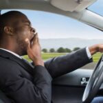 Side View Of A Young African Businessman Yawning While Driving Car